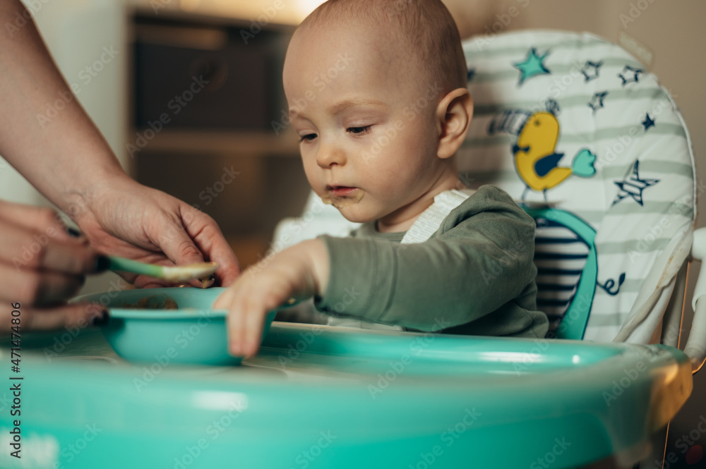 Baby eating with a face stained in food while mother feeds him with a spoon Baby eating with a face stained in food while mother feeds him with a spoon