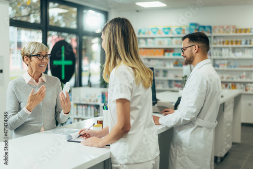 Two pharmacist giving prescription medications to senior female customer in a pharmacy photo