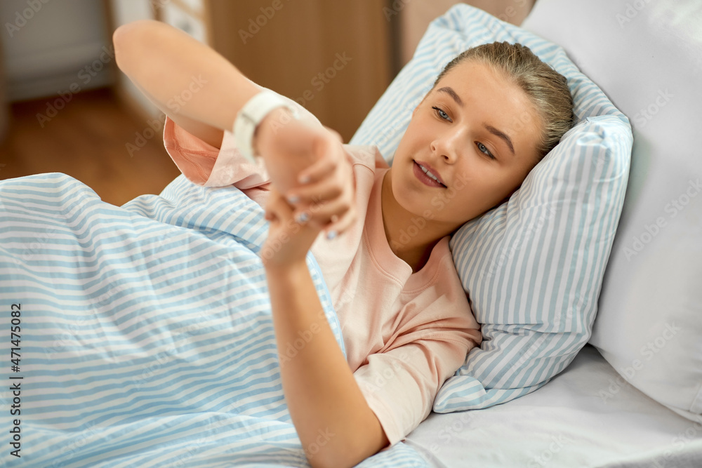 people, health and sleeping concept - happy smiling awake girl lying in bed at home and looking at wristwatch people, health and sleeping concept - happy smiling awake girl lying in bed at home and looking at wristwatch