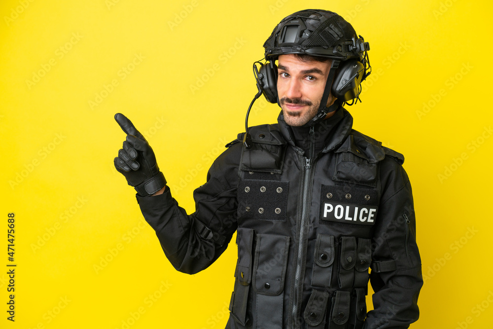 SWAT caucasian man isolated on yellow background pointing finger to the side SWAT caucasian man isolated on yellow background pointing finger to the side