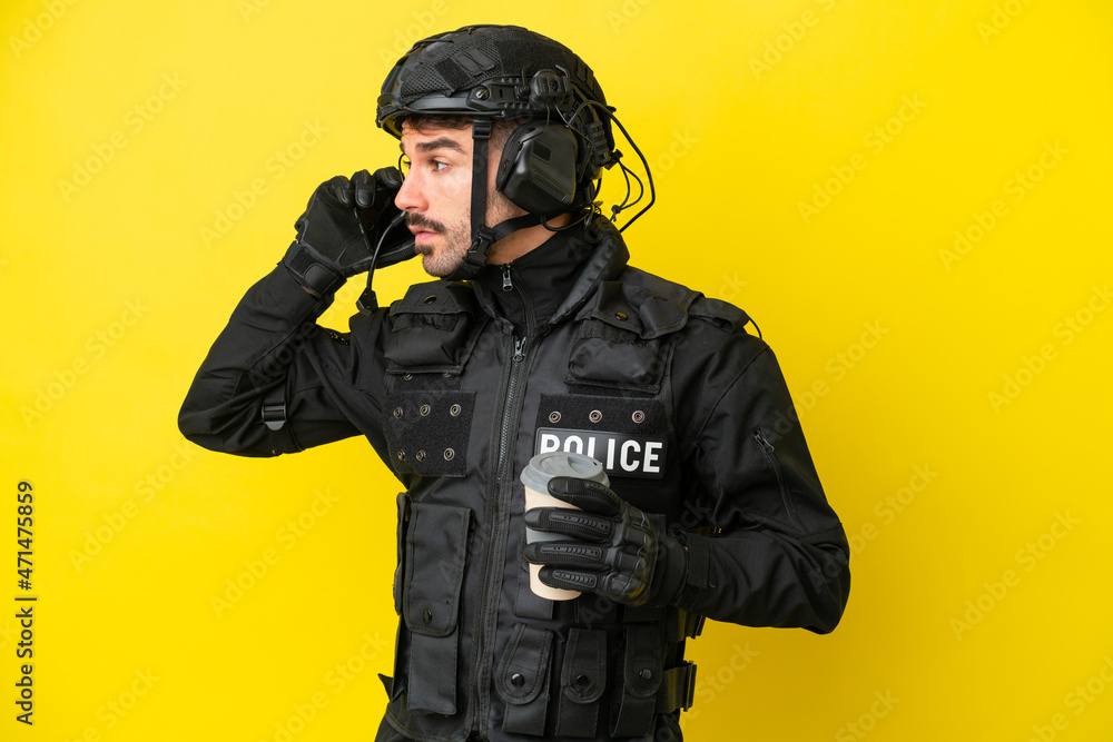 SWAT caucasian man isolated on yellow background holding coffee to take away and a mobile SWAT caucasian man isolated on yellow background holding coffee to take away and a mobile