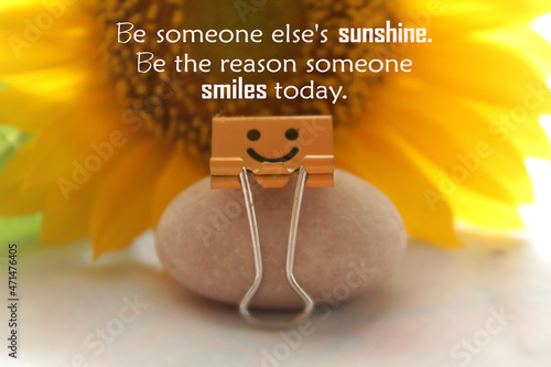 Kindness inspiraitonal quote - Be someone else's sunshine. Be the reason someone smiles today. With orange smiling paper clip sitting on a stone on sunflower background on the table. Words of wisdom. photo