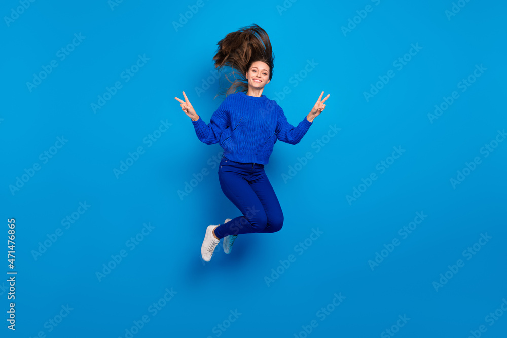 Full length body size view of attractive cheery girl jumping showing v-sign having fun isolated on bright blue color background