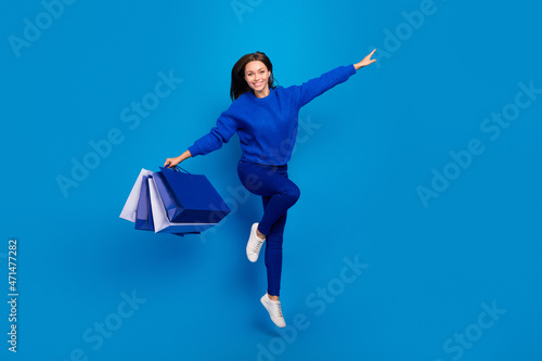 Full length body size view of attractive cheerful girl jumping carrying gifts isolated on bright blue color background