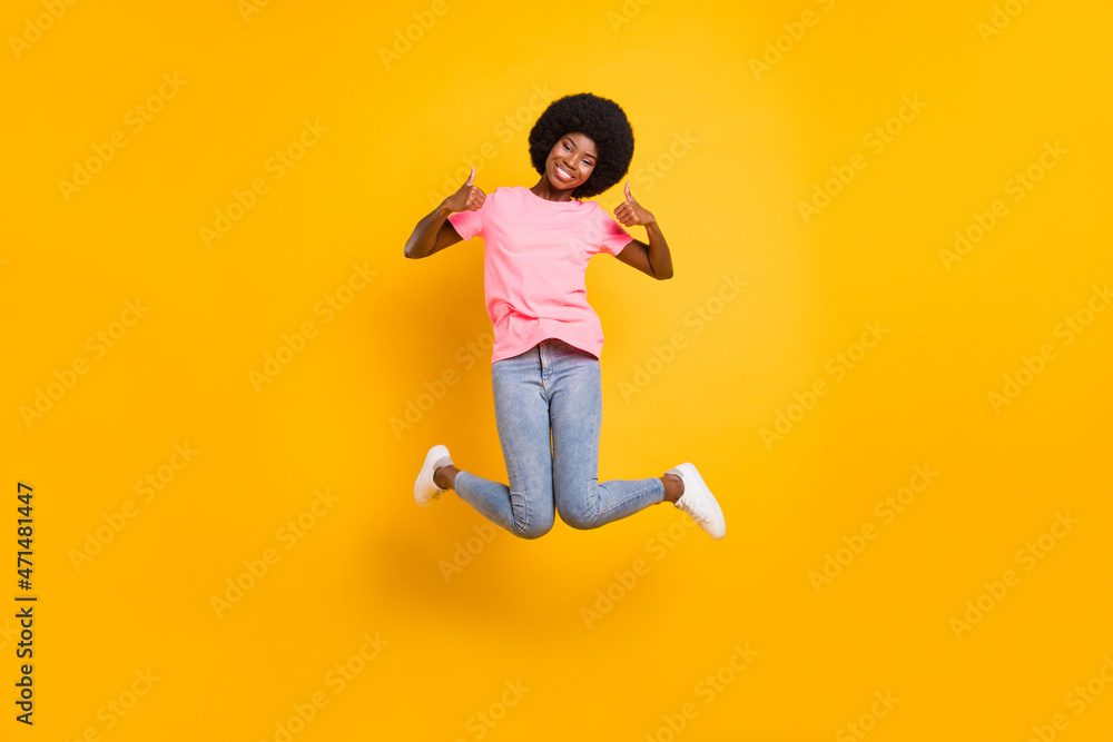 Full size photo of cool millennial lady jump show thumb up wear pink t-shirt jeans isolated on yellow color background