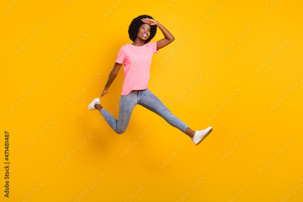 Full size photo of interested millennial lady jump look wear pink t-shirt jeans isolated on yellow color background Full size photo of interested millennial lady jump look wear pink t-shirt jeans isolated on yellow color background