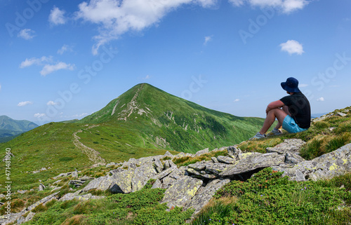 A man in a black hat sits on the slope of the Montenegrin ridge in the Carpathians and looks at Hoverla, the highest mountain in Ukraine