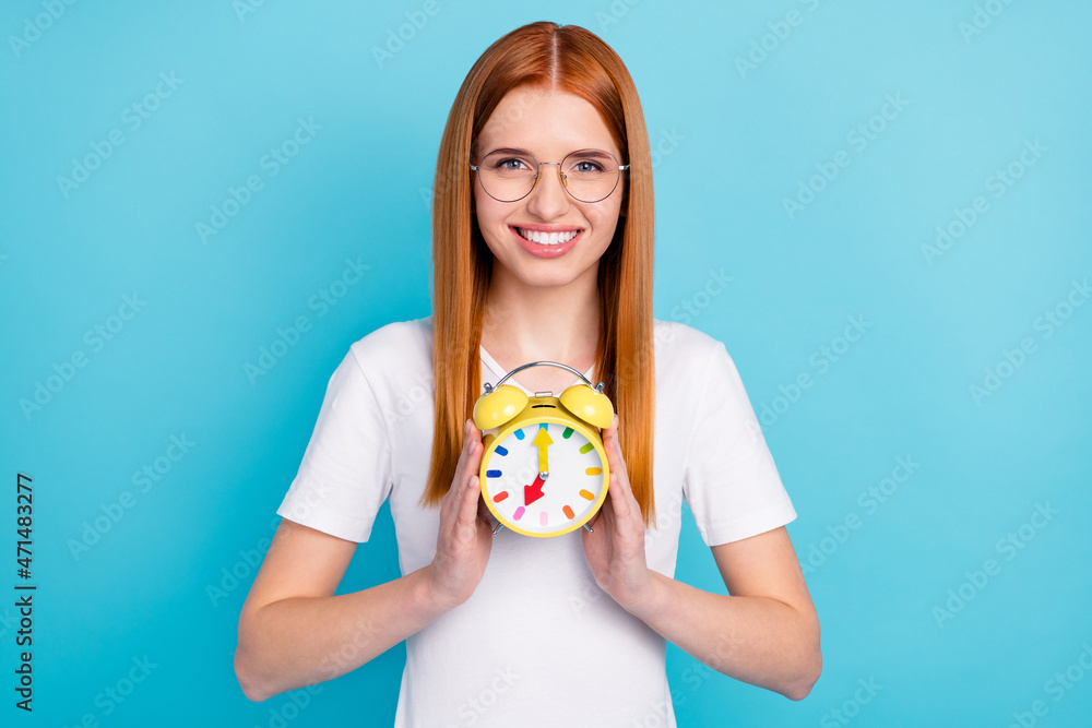 Photo of young attractive girl happy positive smile hold clock timer isolated over blue color background Photo of young attractive girl happy positive smile hold clock timer isolated over blue color background