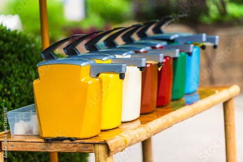 A line of colorful condiment containers/dispensers at an outdoor restaurant.