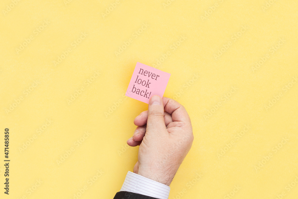 The hand holds a sticky note with inscription Never look back The hand holds a sticky note with inscription Never look back