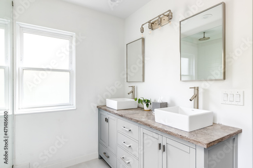An elegant, renovated bathroom with white sinks, grey vanity, granite countertop, and bronze hardware, faucets and light. 