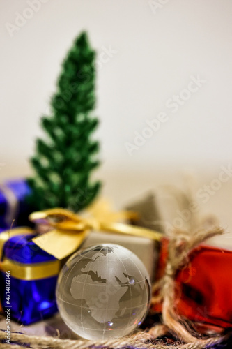 Merry Christmas, Happy New Year and Boxing day concept. Present boxes, world gloge crystal glass, pine tree and house models on light brown background. © Eve