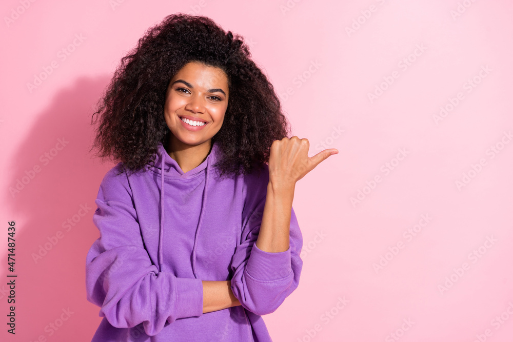 Photo of pretty charming afro girl wear violet sweatshirt pointing thumb empty space smiling isolated pink color background Photo of pretty charming afro girl wear violet sweatshirt pointing thumb empty space smiling isolated pink color background