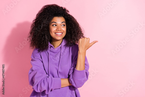 Photo of sweet dreamy african lady dressed purple hoodie smiling looking pointing thumb empty space isolated pink color background