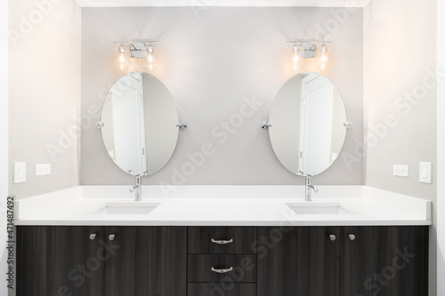 Canvas A luxury bathroom with a wooden vanity cabinet, large marble countertop, and lights mounted above circular mirrors