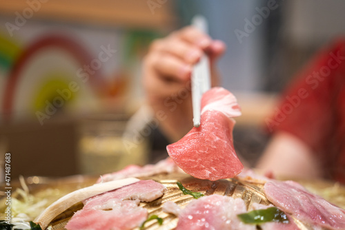 Action of people hand using chopstick to grilling a piece of slice pork meat in BBQ meal. Eating food close-up action photo. Selective focus.