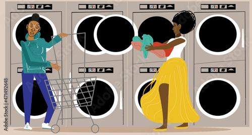 Lesbian couple in the laundromat while partner pushes laundry cart 