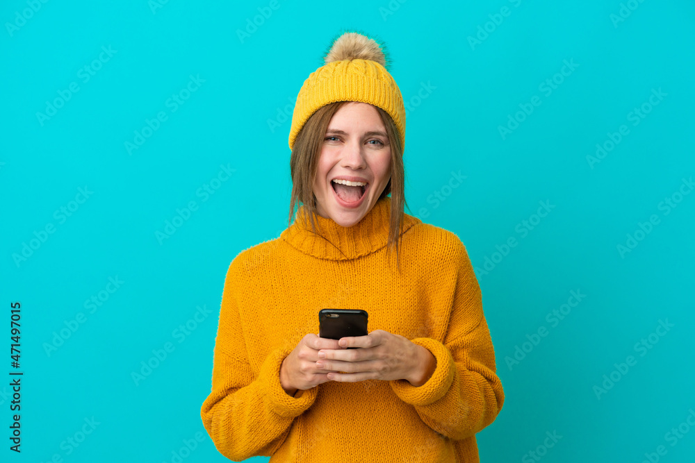 Young English woman wearing winter jacket isolated on blue background surprised and sending a message Young English woman wearing winter jacket isolated on blue background surprised and sending a message