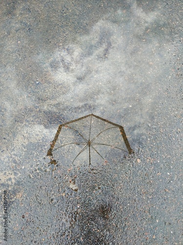 Weightless reflection of an umbrella and clouds in a puddle on the asphalt road
