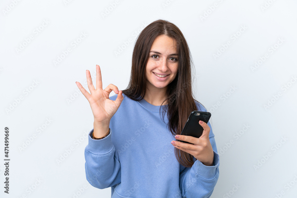 Young Ukrainian woman isolated on white background using mobile phone and doing OK sign Young Ukrainian woman isolated on white background using mobile phone and doing OK sign
