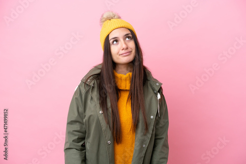 Young Ukrainian woman wearing winter jacket isolated on pink background and looking up