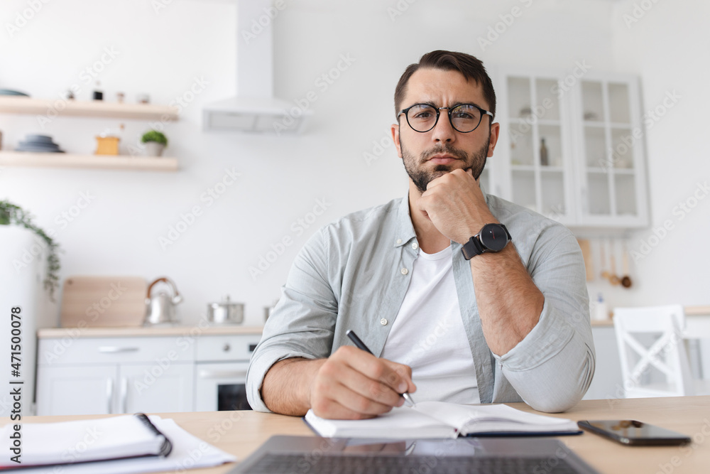 Thoughtful middle aged caucasian man student with beard in glasses works at laptop and watch online lesson Thoughtful middle aged caucasian man student with beard in glasses works at laptop and watch online lesson