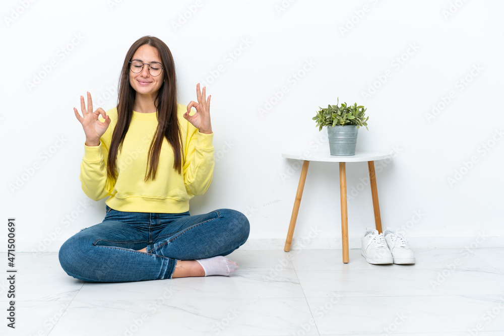 Young Ukrainian woman sitting on the floor of her house isolated on white wall in zen pose Young Ukrainian woman sitting on the floor of her house isolated on white wall in zen pose
