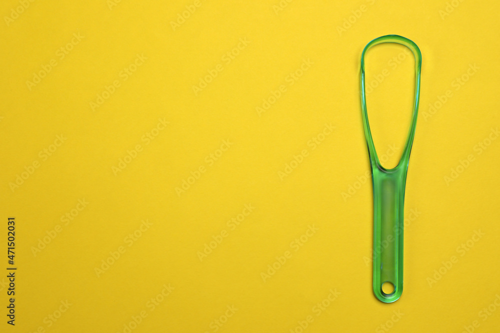 Green tongue cleaner on yellow background, top view. Space for text Green tongue cleaner on yellow background, top view. Space for text