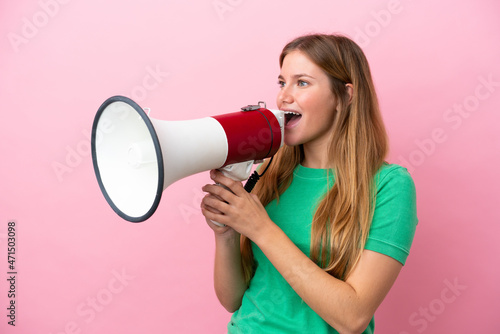 Young blonde woman isolated on pink background shouting through a megaphone to announce something in lateral position