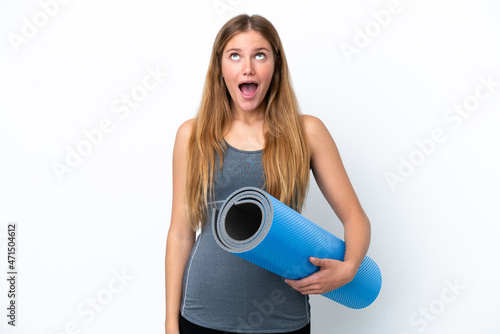 Young sport woman going to yoga classes while holding a mat looking up and with surprised expression