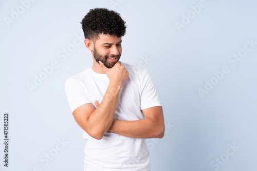 Young Moroccan man isolated on blue background looking to the side and smiling