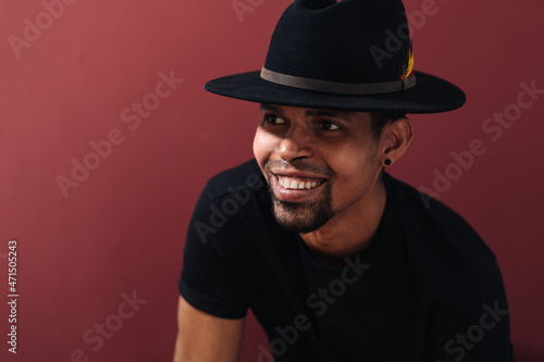 Portrait of handsome young African man smiling in black t-shirt and hat on burgundy background