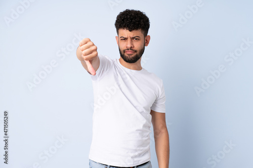 Young Moroccan man isolated on blue background showing thumb down with negative expression