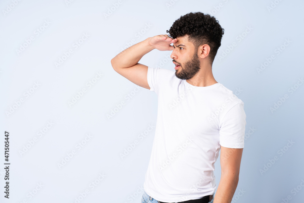 Young Moroccan man isolated on blue background with surprise expression while looking side Young Moroccan man isolated on blue background with surprise expression while looking side