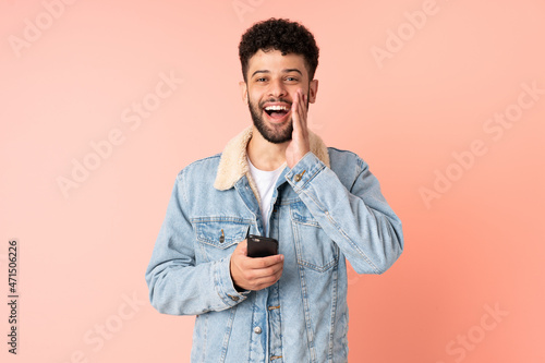 Young Moroccan man using mobile phone isolated on pink background with surprise and shocked facial expression © luismolinero