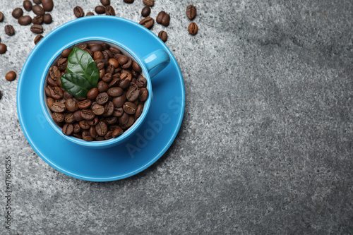 Cup with roasted coffee beans and leaves on grey table, flat lay. Space for text
