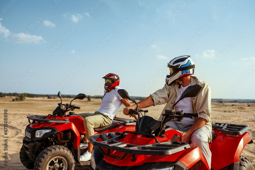 Two men in helmets ride on atv in desert Two men in helmets ride on atv in desert