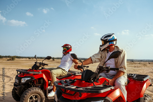 Two men in helmets ride on atv in desert