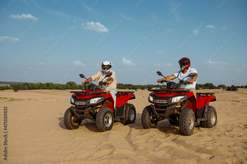 Obraz premium Men in helmets and glasses ride on atv in desert