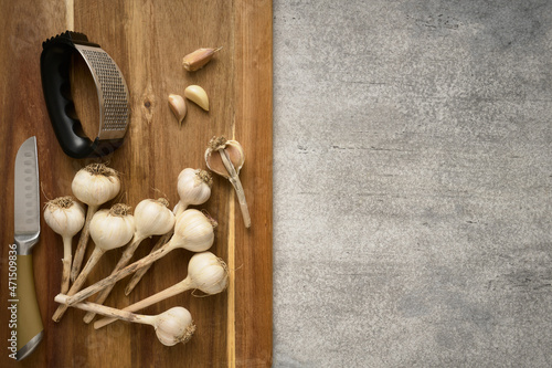 Wooden cutting board with garlic heads and garlic press, close up