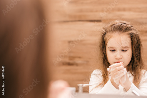 Personal hygiene. A little girl in front of the mirror washes and brushes her teeth.