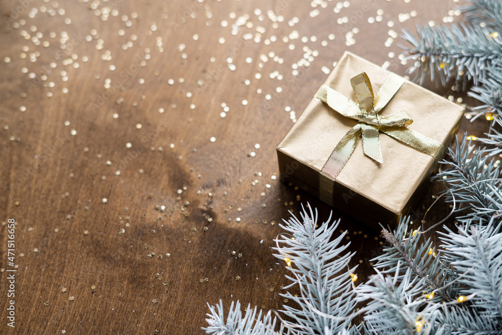 a golden gift box on a wooden table among fir branches with warm light bulbs