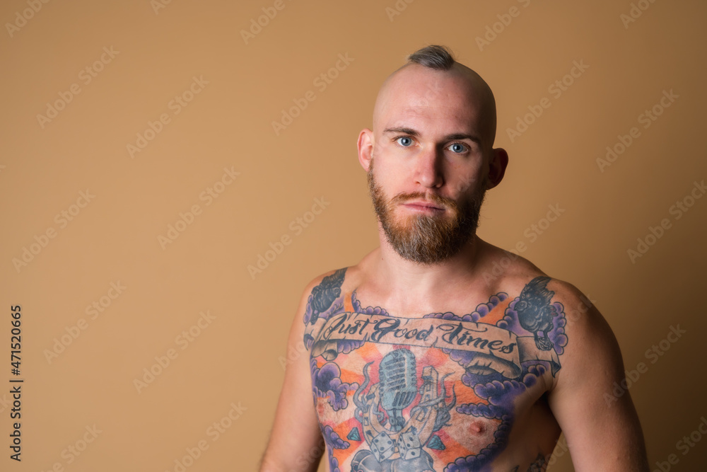 Tattooed brutal man with beard, topless naked on beige background, muscular with abs Tattooed brutal man with beard, topless naked on beige background, muscular with abs