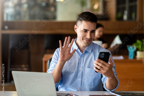 Businessman video call with clients on smartphone waving at screen.