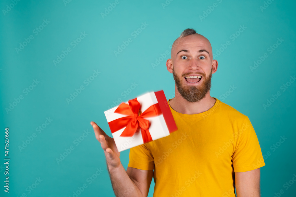 A bearded man in an orange T-shirt on a turquoise background throws a gift box in an elated mood, gives joy, smiles pleasantly A bearded man in an orange T-shirt on a turquoise background throws a gift box in an elated mood, gives joy, smiles pleasantly