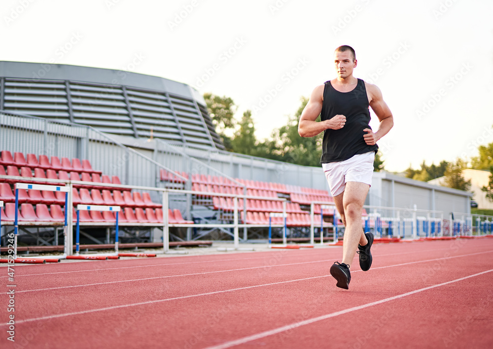 Fototapeta premium Young muscular fit male sprinter running on a red running track - Fitness and wellness concept with a millennial runner - Copyspace on the photo's left side