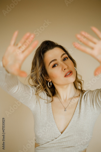 young caucaisan woman extends her arms out in front of her, beauty girl looks forward and puts her palms out, portrait of a young european lady at the beige wall, who puts her hands out in front of