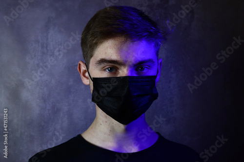 handsome teenage boy in protective medical mask on a gray background in blue neon light
