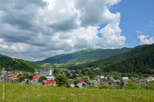 Panoramic view of mountain village Kolochava. Rural landscape with green field, trees, houses and mountains on background. Carpathian Mountains, Transcarpathia, Ukraine.