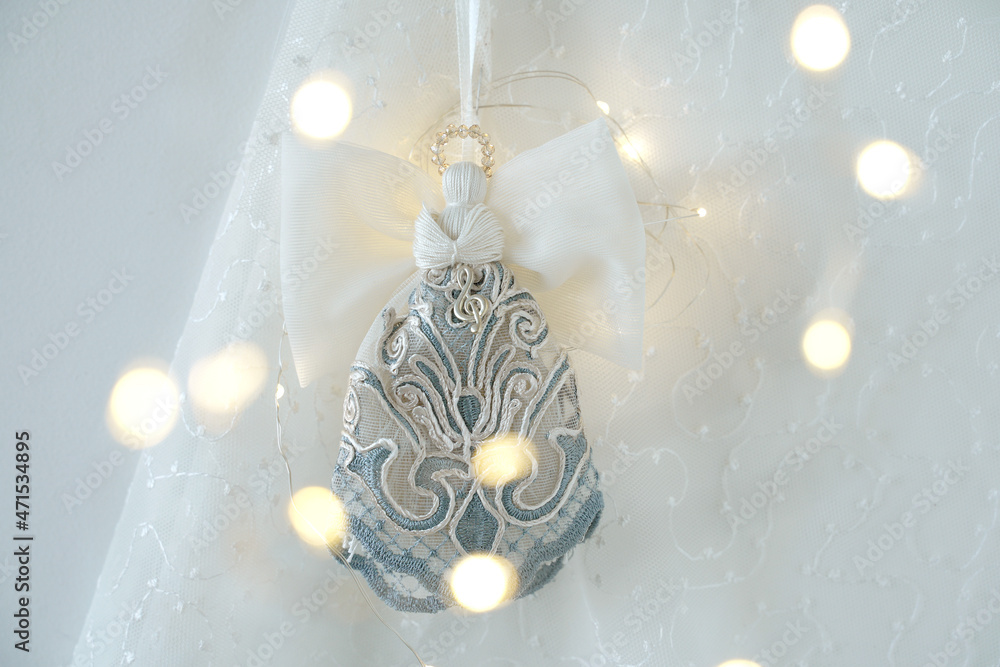Handmade Christmas angel with a musical key on a light background with blurred garland lights.  Christmas decoration on the wall.